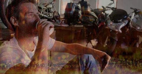 Man relaxing in motorcycle garage with coffee and smartphone