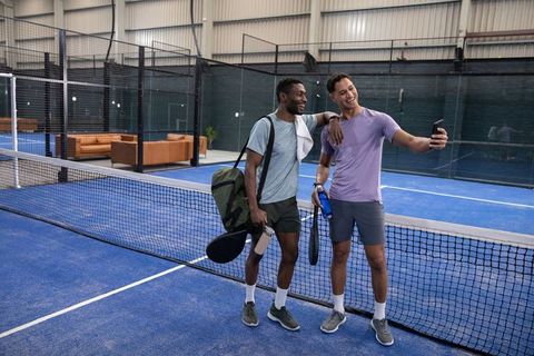 Taking selfie after padel match on indoor blue court with friends