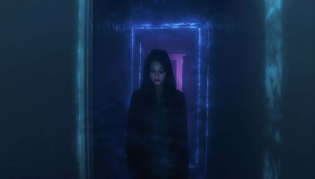 Standing hooded woman gazing downward in neon-lit corridor with glowing portal, cinematic