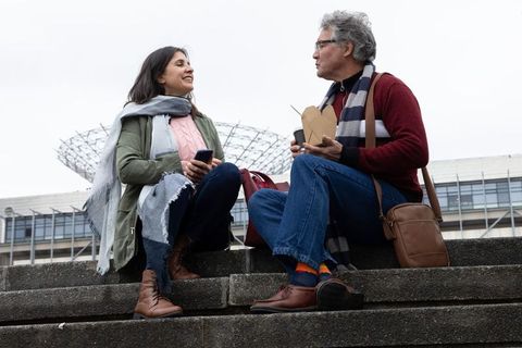 Middle-aged couple sharing outdoor lunch and chatting on city steps near modern building