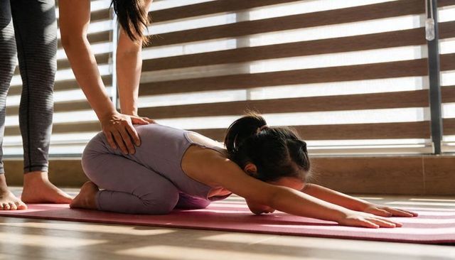 Child practicing yoga in child pose with instructor guiding gentle stretch