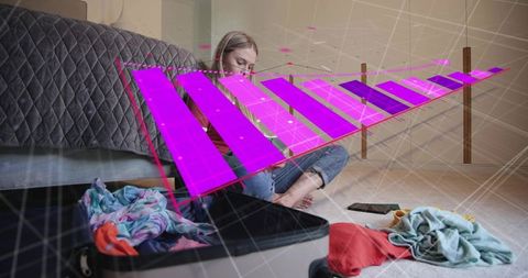Young woman packing clothes on bedroom floor with augmented reality travel data overlay