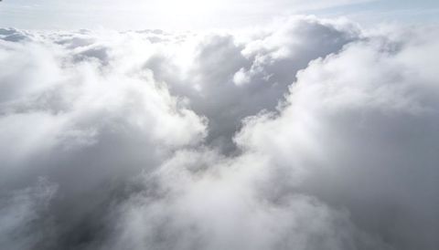 Sunlit cumulus sea from high altitude — aerial cloudscape with light, shadow and misty horizon