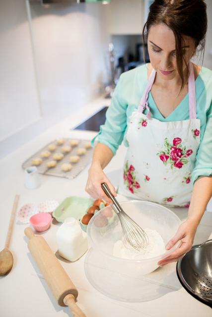 Beautiful woman whisking flour in bowl at kitchen