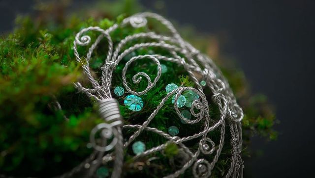Turquoise beaded silver filigree wirework resting on lush green moss macro