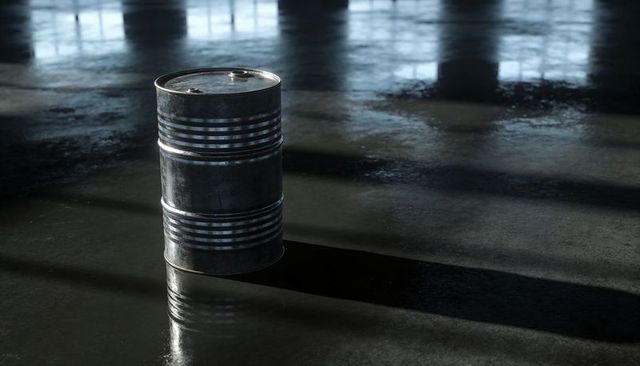Rusty steel drum casting long shadow on wet concrete floor with window reflections