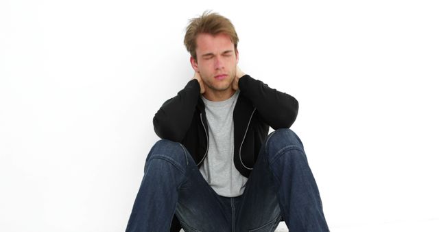 Young Man Sitting Against White Wall Holding Neck in Pain - Download Free Stock Images Pikwizard.com