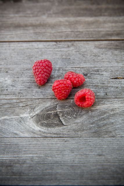 Fresh red raspberries scattered on rustic wooden table represent healthy, organic food. Ideal for concepts related to natural living, simple lifestyles, and nutritional meals. Suitable for food blogs, healthy living articles, and advertisements for organic products.