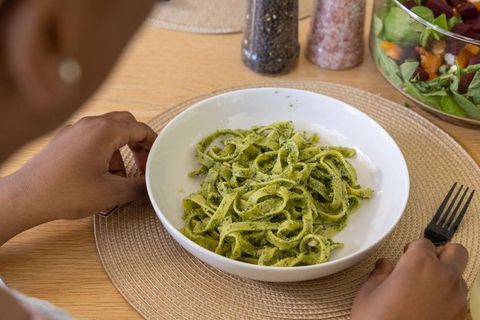 Teenage female reaching for fork with pesto fettuccine on wooden table