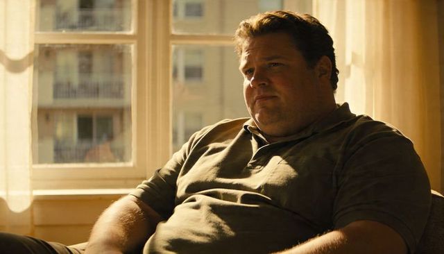 Sunlit man sitting in armchair gazing through multi-pane window with sheer curtains