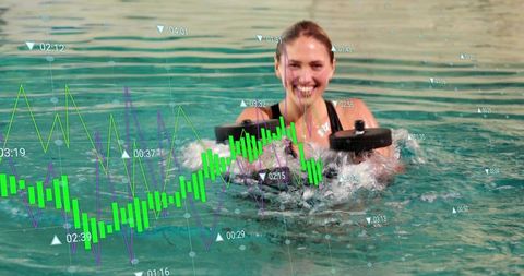 Smiling woman lifting foam dumbbells in pool splashing, augmented data charts floating