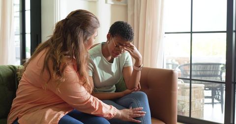 African American woman comforting distressed friend on sofa in sunlit living room