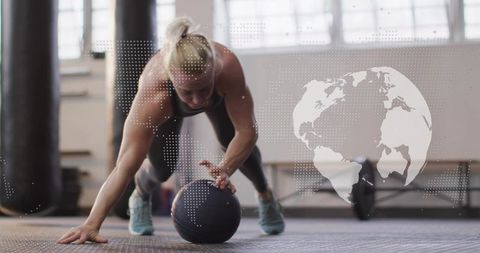 Female athlete performing plank with medicine ball in industrial gym studio