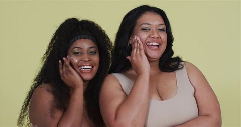 Diverse females skincare applying cream smiling yellow background