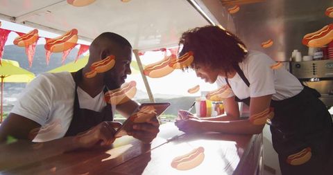 Food truck team working together writing orders and checking tablet in sunny outdoor market