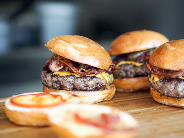 Three delicious bacon cheeseburgers are displayed on a wooden plank. The buns are slightly toasted, with visible layers of beef patties, melted cheese, and crispy bacon. Perfect use for marketing campaigns for fast food restaurants, menu designs, online food delivery services, and social media posts promoting comfort food and gourmet burgers.