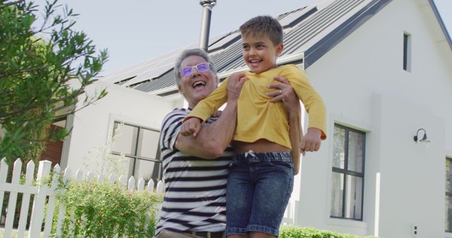 Grandfather Lifting Grandson in Front of Modern House with Solar Panels - Download Free Stock Images Pikwizard.com