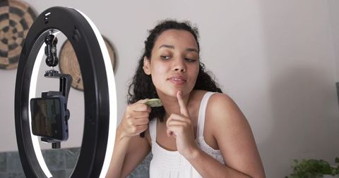 Content creator demonstrating gua sha facial routine with led ring light and smartphone