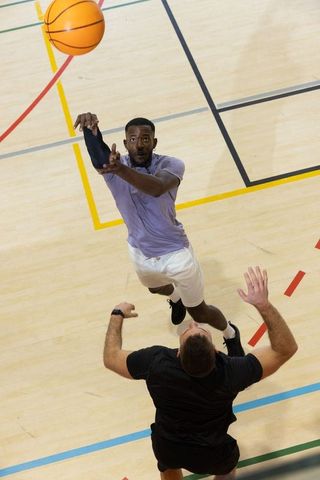 Diverse male basketball players leaping and shooting over defender on hardwood court