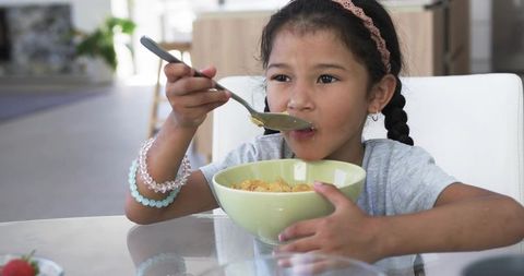 Young Girl Eating Breakfast Cereal at Home Morning Routine Enjoying Bowl at Glass Table
