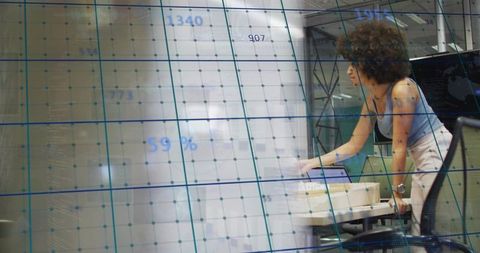 Leaning professional checking laptop with translucent data grid overlay in modern office