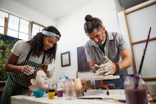 Man and woman engaged in pottery class, sculpting and painting clay figures. Ideal for use in educational materials, creative workshops, hobby promotion, and artistic skill development content.