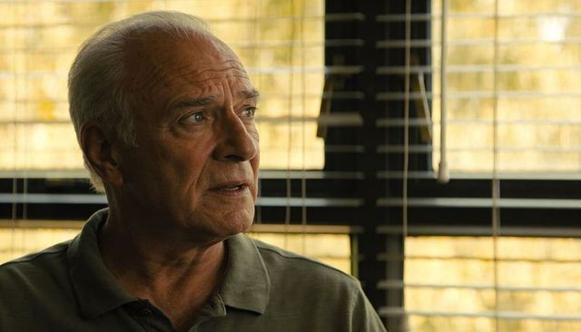 Senior man sitting by sunlit window contemplating life, warm portrait with blinds