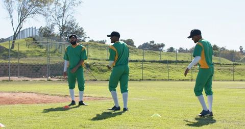 Diverse baseball teammates practicing throws and drills on sunny outfield in green uniforms