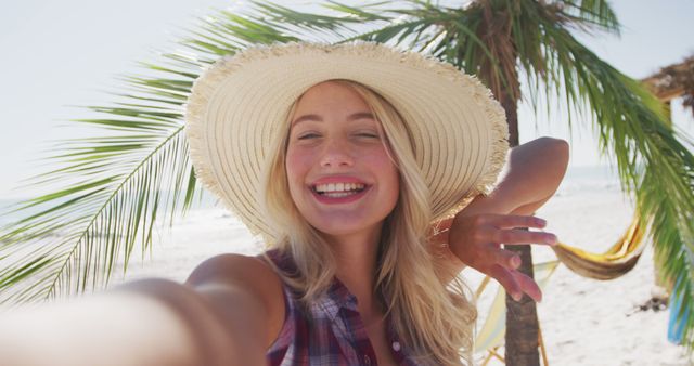 Smiling woman in straw hat taking selfie on a beautiful tropical beach, ideal for promoting vacation destinations, summer holidays, and travel joy. Perfect for travel blogs, beach vacation advertisements, and social media content celebrating tropical getaways.