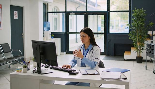 Female doctor conducting virtual consultation at desk with computer and clipboard