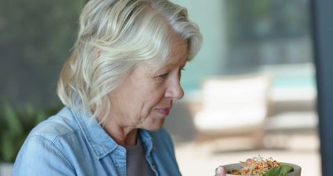 Senior woman enjoying fresh salad while sitting by window embracing healthy lifestyle
