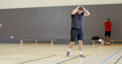 Basketball player holding head on indoor court while teammate cheering from bench