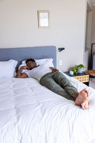 African american man resting on made bed in minimalist contemporary bedroom with plant