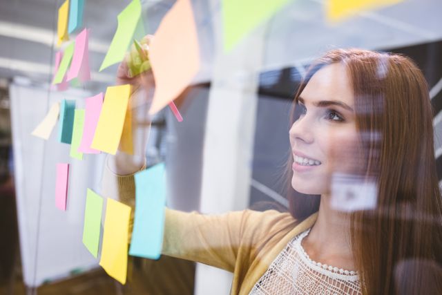 Attractive businesswoman writing on sticky notes in creative office 