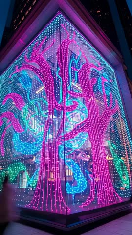 Vertical neon LED vines animating glass facade in urban plaza with passing pedestrians