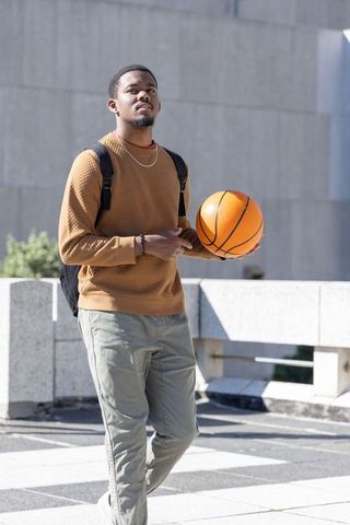 African american man holding basketball on sunlit urban rooftop with backpack