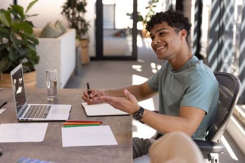 Hispanic male writing and conversing in coworking space