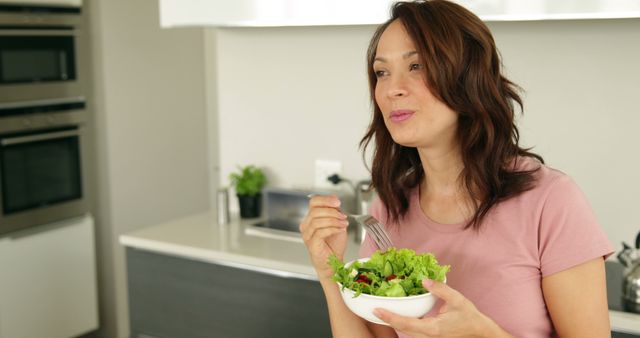 Pretty woman eating a bowl of healthy salad at home in the kitchen