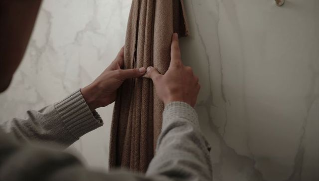 Man adjusting brown towel on hook in marble bathroom close-up of hands and textures