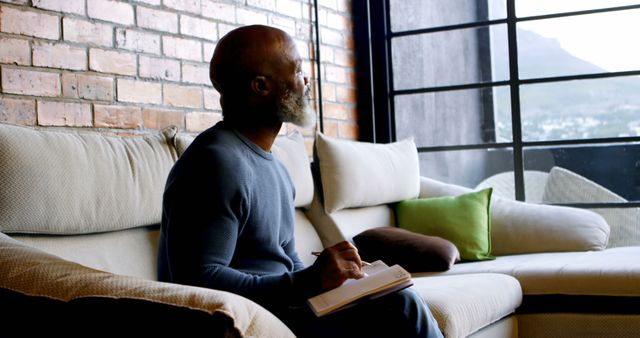 Pensive Man Journaling by Large Window in Cozy Urban Apartment - Download Free Stock Images Pikwizard.com