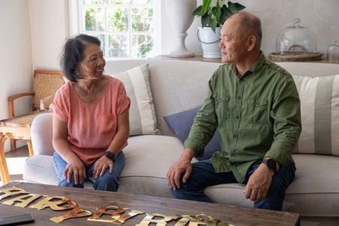 Senior chinese couple chatting on sofa celebrating intimate birthday at cozy sunlit home