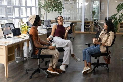 Creative team laughing and collaborating over coffee in modern open-plan office workspace