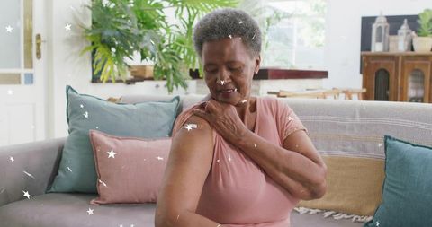 Senior woman touching upper arm revealing adhesive patch while sitting on cozy sofa