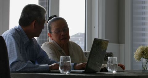 Senior Asian Couple Engaged with Laptop at Home Dining Table