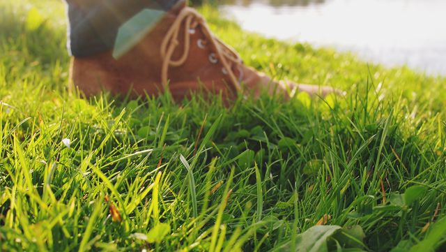 Sunlit green grass surrounding a person wearing brown boots. Ideal for illustrating outdoor activities, nature walks, countryside relaxation, and casual footwear fashion. Suitable for blogs, advertisements, websites, and presentations focusing on outdoor lifestyles, nature appreciation, and comfortable walking.