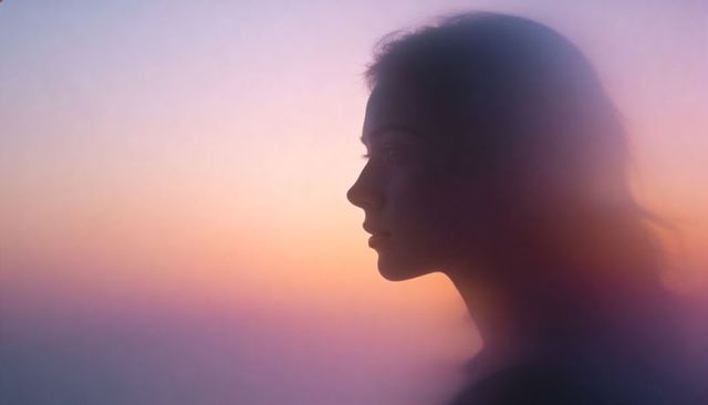 Silhouette of young woman in profile gazing at pastel sunset twilight with dreamy haze