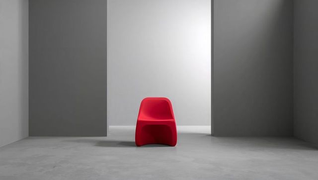 Bright red sculptural chair anchoring minimalist gray studio alcove with soft shadow