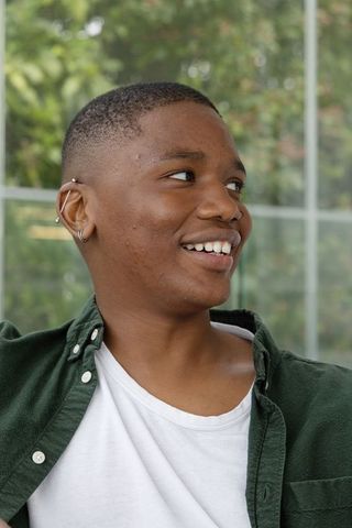 African american teen smiling and looking out window, wearing green shirt and ear piercings