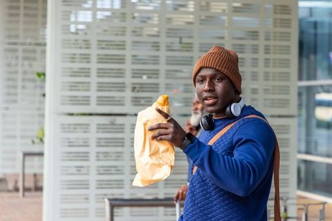 Young african american commuter holding paper bag at transit station wearing headphones