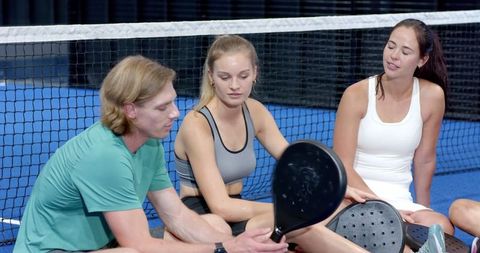 Friends discussing paddle tennis equipment on indoor court